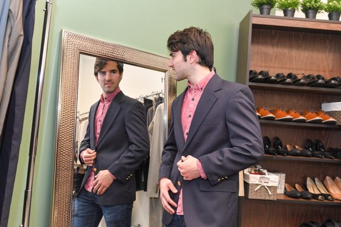male student looks in the mirror while trying on a suit jacket