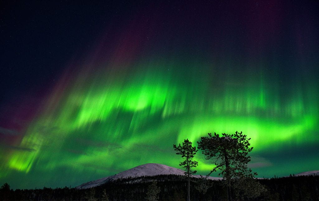 Green and purple bands in a dark sky overlooking a snowy mountain.
