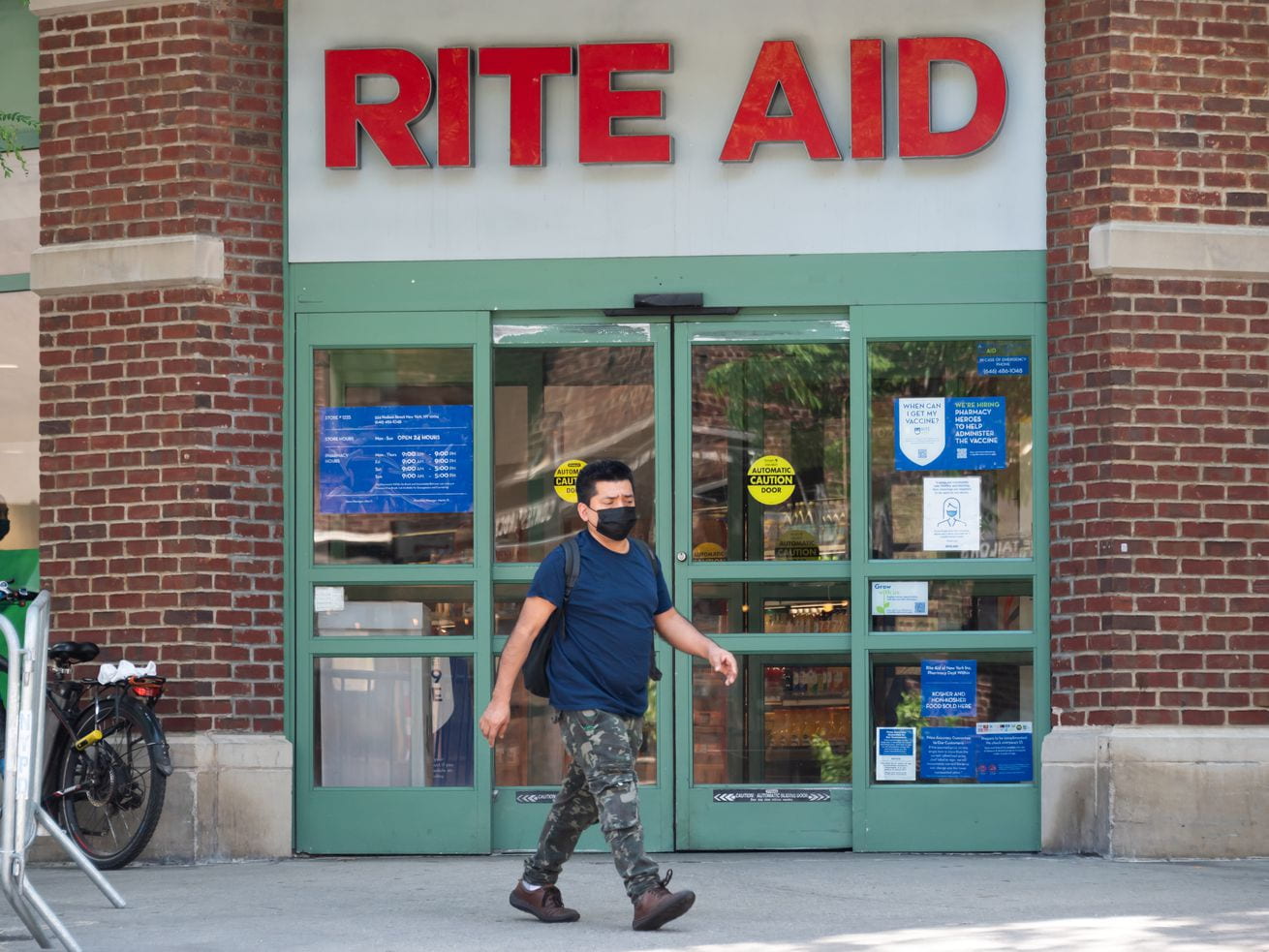 A masked person walks in front of a Rite Aid.
