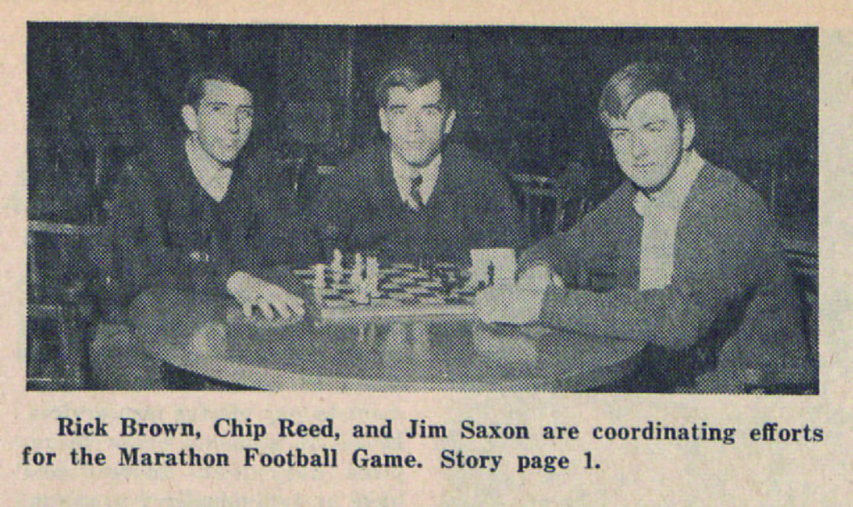 Photograph of three men gathered around a table playing chess. The caption reads Rick Brown, Chip Reed, and Jim Saxon are coordinating efforts for the Marathon Football Game. 